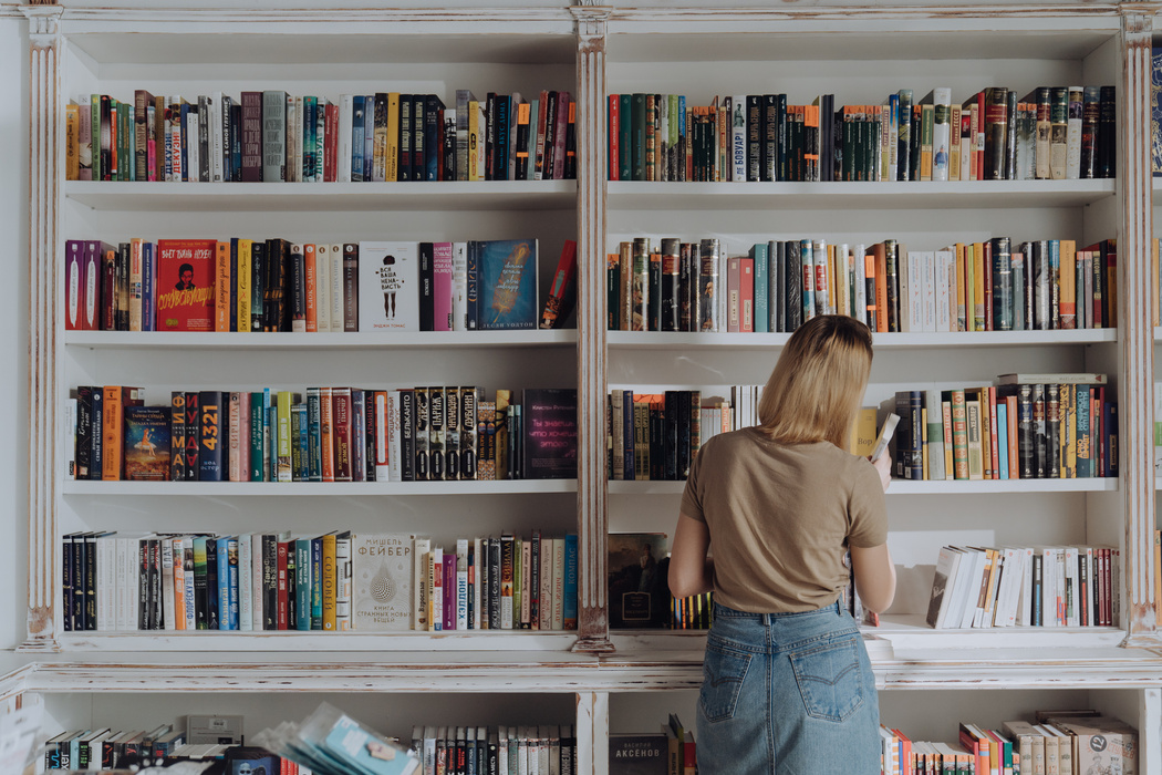 Woman in Beige Shirt and Blue Denim Jeans Standing in Front of Books
