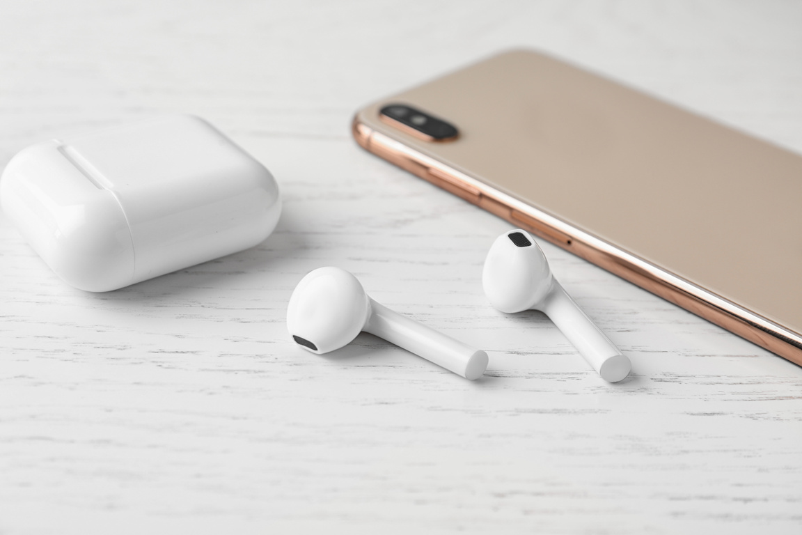 Wireless Earphones, Mobile Phone and Charging Case on White Wooden Table
