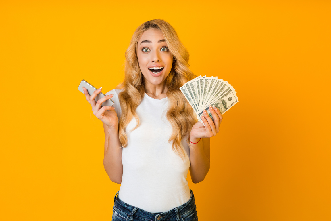 Make money online. Surprised woman holding smartphone and money