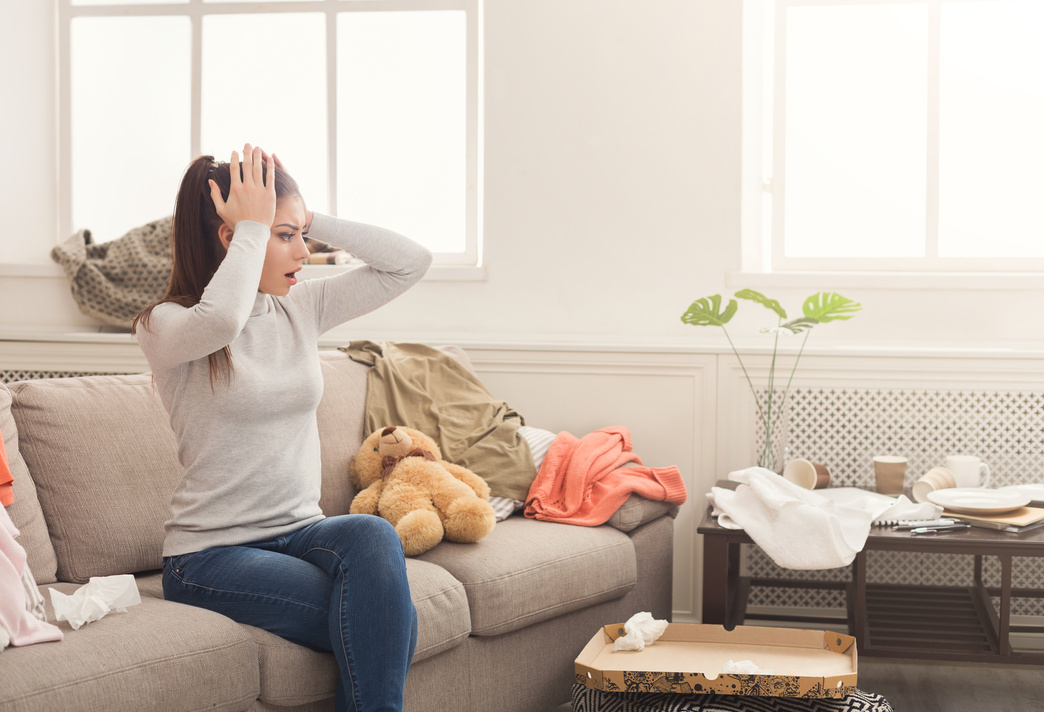 Desperate woman sitting on sofa in messy room