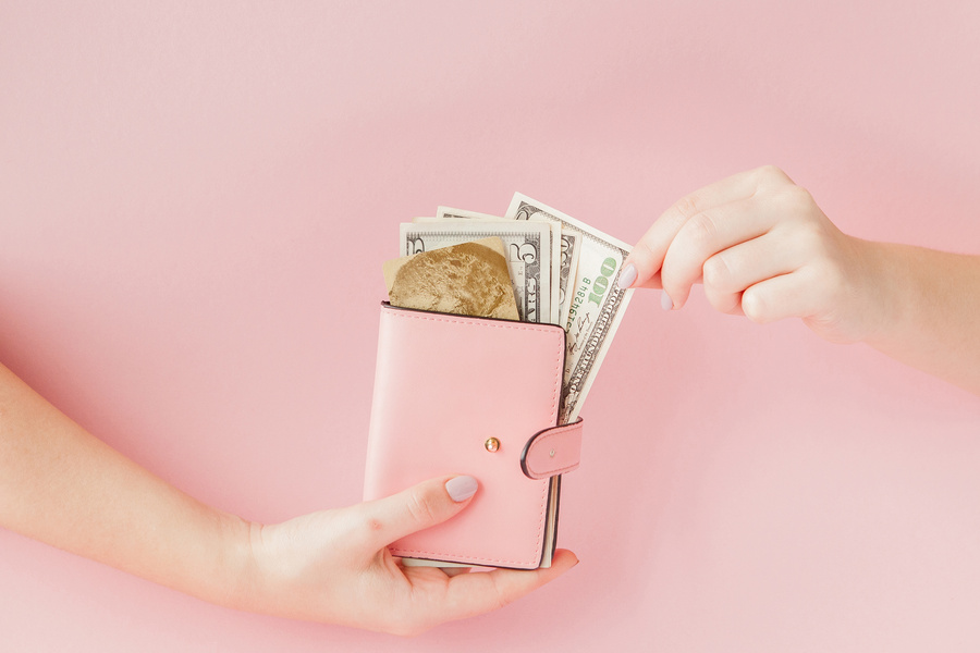 Dollars and pink wallet with credit card in woman's hands on pink background
